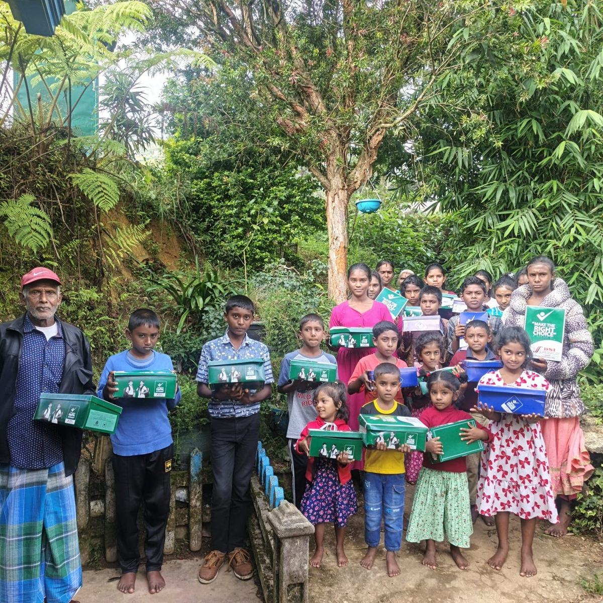 Children and a community elder holding boxes of new shoes in the Sri Lankan highlands